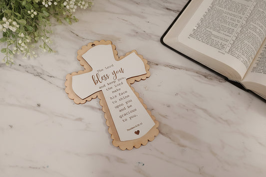 Decorative cross with text on a marble surface next to an open book